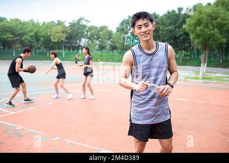 Fröhliche junge chinesische Freunde, die draußen Basketball spielen Stockfoto