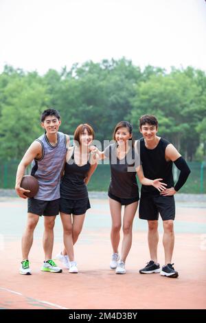 Fröhliche junge chinesische Freunde, die draußen Basketball spielen Stockfoto