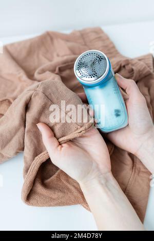 Ein Mädchen entfernt große Spulen aus der Kleidung mit einer elektronischen Maschine. Das Konzept der Kleiderschonung, Spulenreinigung Stockfoto