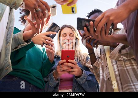 Niedriger Blickwinkel einer Gruppe junger Teenager, die Mobiltelefone benutzen. Konzept von Technologie, Verbindung. Stockfoto