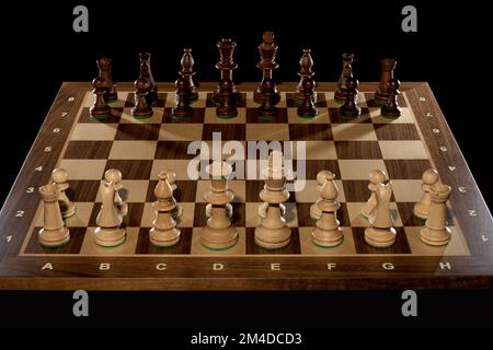 Holzschachbrett mit Stücken in Startposition, dunkler Hintergrund mit Hintergrundbeleuchtung Stockfoto