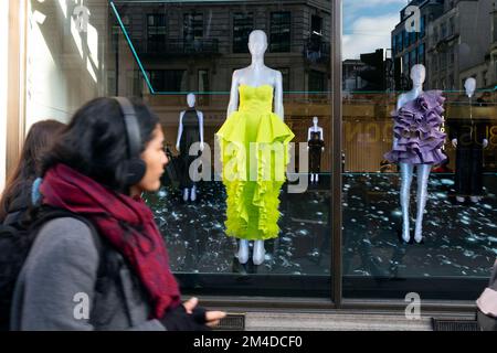 Junge Frau, die im H&M-Schaufenster auf der Regent Street am 2022. Dezember in West End London England UK KATHY DEWITT auf ein lindgrünes Kleid schaut Stockfoto