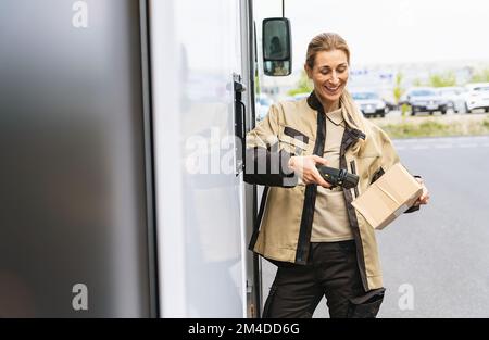 Weibliche Lieferantin scannt den Barcode mit einem Barcode-Scanner außerhalb ihres Lieferwagens auf einem Paket während seiner Schicht Stockfoto