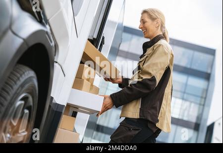 Weibliche Lieferantin, die Pakete von einem Lieferwagen an einen Kunden ausliefert. Konzeptbild „Kurierdienst“ Stockfoto