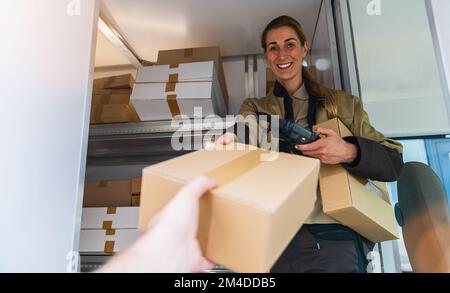 Eine Lieferagentin übergibt ein Paket in ihrem Lieferwagen, um es an einen Kunden zu liefern Stockfoto