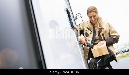Weibliche Lieferantin scannt den Barcode außerhalb ihres Transporters auf einem Paket Stockfoto