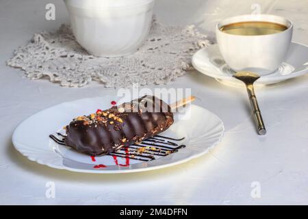Dessertkuchen auf weißem Teller, Nahaufnahme, selektiver Fokus. Kuchen mit Schokolade und Nüssen bedeckt. Stillleben im Stil eines hohen Schlüssels Stockfoto