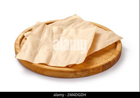 Backpapier auf Holzplatte isoliert. Rundes Brett mit zerknitterten Stücken braunem Pergament oder Backpapier auf weißem Hintergrund. Konstruktionselement. Stockfoto