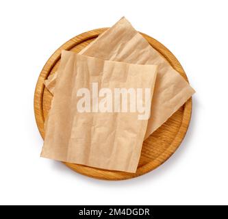 Backpapier auf Holzplatte isoliert. Rundes Brett mit zerknitterten Stücken braunem Pergament oder Backpapier auf weißem Hintergrund. Draufsicht. Design-Element Stockfoto