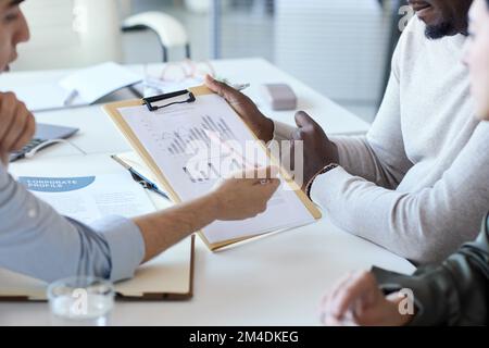Nahaufnahme des Geschäftsteams, das auf das Datendiagramm in der Zwischenablage in der Besprechung zeigt Stockfoto