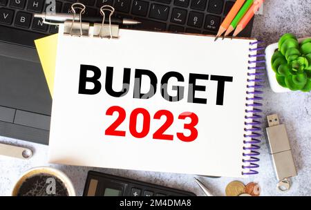 Notizblock mit Text BUDGET 2023, Brille, Büroklammern, weißem Taschenrechner und Stift auf Desktop, Draufsicht Stockfoto