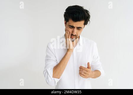 Mittelgroßes Studioporträt eines unglücklichen Mannes mit geschlossenen Augen und schweren Zahnschmerzen, der den Kiefer mit den Fingern berührt, um einen starken Zahn zu lindern Stockfoto