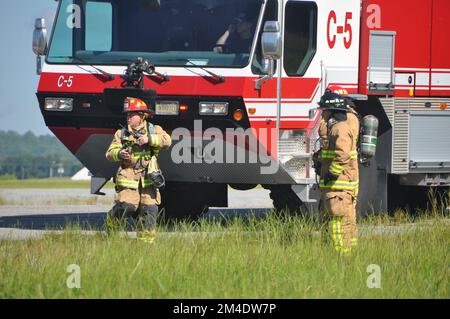 Feuerwehrleute aus der 908.. Bauingenieurschwadron des 908. Airlift Wing und der Feuerwehr von Fort Benning diskutieren, wie ein Hubschrauberbrand angegriffen werden kann, nachdem sie am 4. August 2022 in Fort Benning Georgia bei einem Feuertrainer für ein Hubschrauberflugzeug angekommen sind. Die 908. Feuerwehrmänner führten gemeinsam mit der Feuerwehr von Fort Benning ihre erste gemeinsame Interoperabilitätsschulung durch und setzten den Helikoptertrainer ein, um ihre Ausbildung zur Vorbereitung auf die 908 AW-Remission zur formellen Trainingseinheit der Air Force für den MH-139A Grey Wolf Hubschrauber zu beschleunigen. (USA Air Force Foto von Bradley J. Stockfoto