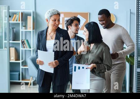 Fröhliche, multiethnische Gruppe von Geschäftsleuten mit leitender Chefin, die im Büro auf die Kamera zugeht Stockfoto
