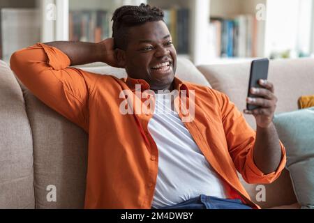Glücklicher, entspannter Schwarzer, der sich Videos auf dem Smartphone ansieht Stockfoto