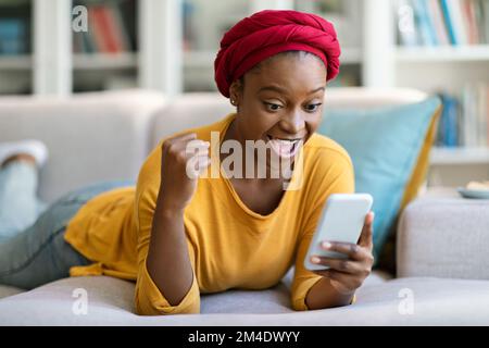 Lächelnde afroamerikanische Frau mit Smartphone zu Hause Stockfoto
