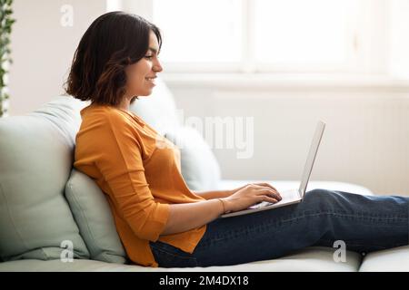 Side View-Aufnahme Einer Jungen Arabischen Frau, Die Auf Dem Sofa Mit Einem Laptop Sitzt Stockfoto