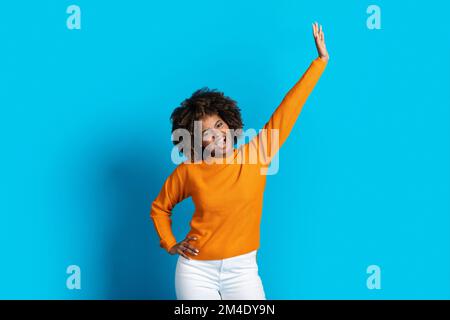Fröhliche afroamerikanische junge Frau, die sich auf Blau bewegt Stockfoto