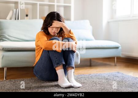 Porträt Einer Aufgebrachten Jungen Arabischen Frau, Die Zu Hause Auf Dem Boden Sitzt Stockfoto