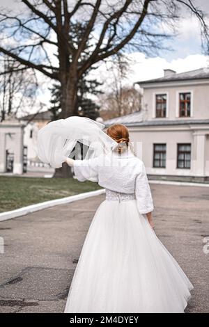 Ein vertikales Bild der Braut, die den Schleier in einem wunderschönen weißen Hochzeitskleid winkt Stockfoto