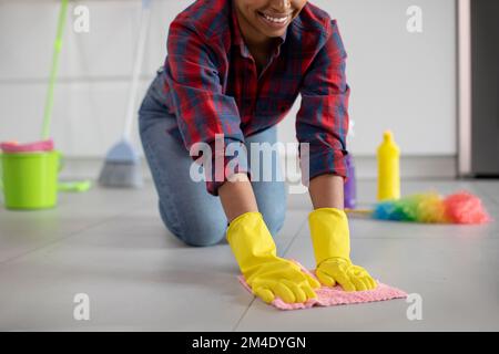 Lächelnde afroamerikanische Hausfrau in Gummihandschuhen wäscht den Boden in der Küche, aus nächster Nähe Stockfoto