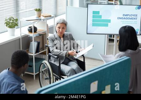 Hochwinkelporträt einer im Rollstuhl tätigen älteren Geschäftsfrau bei der Präsentation im Büro Stockfoto