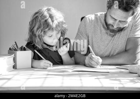 Bärtiger Vater schreibt Schulaufgaben mit seinem Sohn im Klassenzimmer, zurück zur Schule Stockfoto