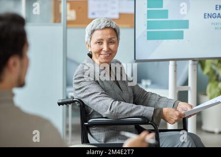 Porträt einer lächelnden Seniorin im Rollstuhl während der Präsentation im Meeting Stockfoto