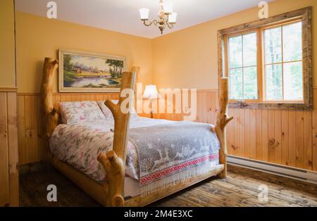 Rustikales Himmelbett im oberen Gästeschlafzimmer mit nuancierten braunen Buntböden im Blockhaus. Stockfoto