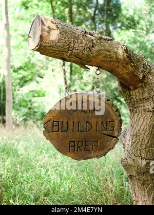 Ein vertikales Bild eines Holzschilds mit dem Text „Den Building Area“, der an einem Baumstamm in einem Wald hängt Stockfoto