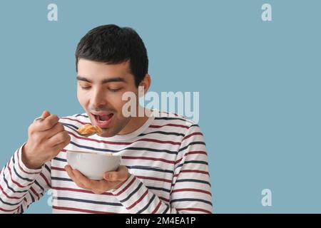 Junger Mann isst Cornflakes mit Löffel auf farbigem Hintergrund, Nahaufnahme Stockfoto