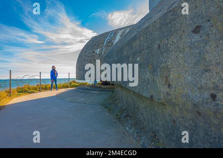 Eine alleinstehende Frau vor einem Bunker mit deutschen Waffen in Omaha Beach, Normandie, Frankreich Stockfoto