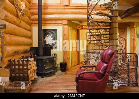 Roter Ledersessel und spiralförmiges Holz und schmiedeeiserne Treppe im Wohnzimmer im 2003 erbauten Cottage-Stil-Blockhaus. Stockfoto