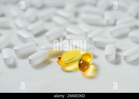 Weiße Tabletten mit einer gelben goldenen Kapsel, die sich von den anderen vor weißem Marmorhintergrund abhebt, Konzept der gesunden Ernährung, Pillen Stockfoto