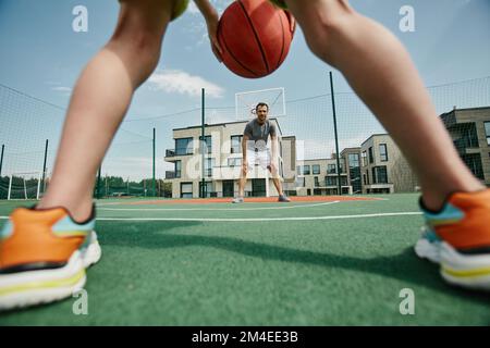 Vater und Sohn, die Basketball spielen, durch die Beine der Jungen geschossen, den Ball verteidigen, Kopierraum Stockfoto