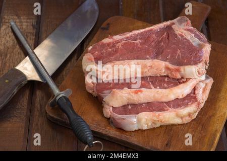 Rohe argentinische Steaks auf einem Holzbrett mit Messer und schärfendem Stahl. Stockfoto