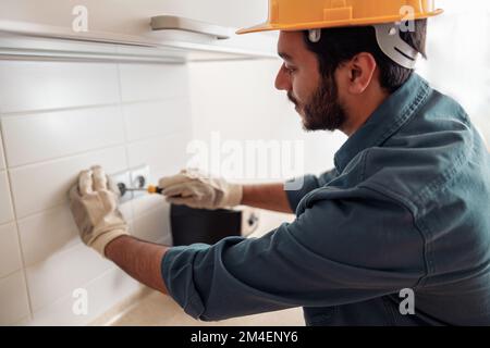 Ein professioneller Elektriker mit Schraubendreher repariert die Steckdose in der Küche Stockfoto