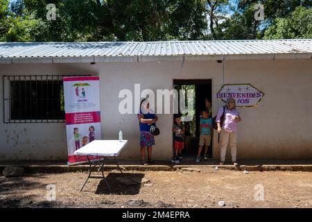 La Labor, La Libertad, Salvador - 27. Oktober 2022 - salvadorianische Frauen und Kinder an einem Eingang mit einem Schild mit der Aufschrift „Welcome“ Stockfoto