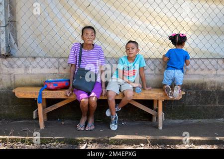 La Labor, La Libertad, Salvador - 27. Oktober 2022 - Alte salvadorianische Frau mit ihren Enkelkindern, die auf einer Bank sitzen und in die Kamera schauen Stockfoto