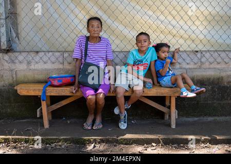 La Labor, La Libertad, Salvador - 27. Oktober 2022 - Alte salvadorianische Frau mit ihren Enkelkindern, die auf einer Bank sitzen und in die Kamera schauen Stockfoto