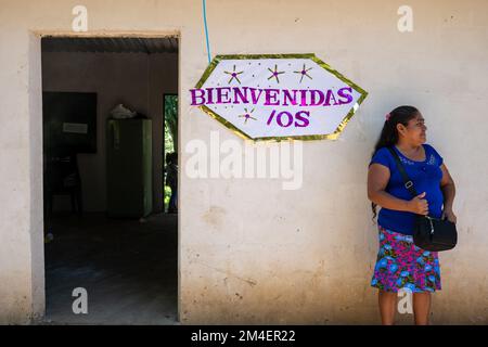 La Labor, La Libertad, Salvador - 27. Oktober 2022 - salvadorianische Frau wartet an einem Eingang mit einem Schild mit der Aufschrift „Welcome“ Stockfoto