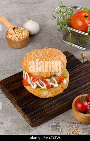 Hausgemachter Hamburger mit Rindfleisch, Zwiebeln, Tomaten, Salat und Käse. Frische Burger auf einem rustikalen Holztisch mit Kartoffelpommes und Pommes frites. Stockfoto