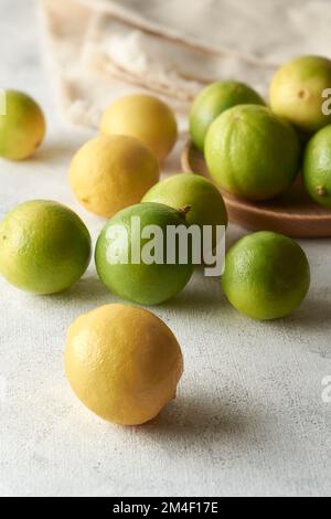 Auf der weißen Tischplatte verstreute Limetten, reich an Vitamin C, Antioxidantien und anderen Nährstoffen, saure Zitrusfrüchte mit selektivem Fokus und verschwommenem Hintergrund, Stockfoto