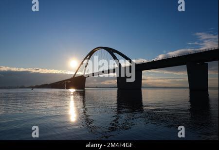 Fehmarn, Deutschland. 16.. Dezember 2022. Die Fahrzeuge fahren über die Fehmarnsund-Brücke unter blauem Himmel. Die Arbeiten an der Baustelle für den geplanten Ostsee-Tunnel in der Nähe von Puttgarden auf der Insel Fehmarn gehen voran. Der 18 km lange Straßen- und Eisenbahntunnel verbindet die Insel Fehmarn mit der dänischen Insel Lolland ab 2029. Laut Femern A/S belaufen sich die Kosten auf 7,1 Milliarden Euro. Kredit: Christian Charisius/dpa/Alamy Live News Stockfoto