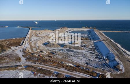 Fehmarn, Deutschland. 16.. Dezember 2022. Die Ausgrabungsgrube für das Tunnelportal zum Fehmarnbelt-Tunnel ist neben dem funktionierenden Hafen und dem Fährhafen von Puttgarden zu sehen (Luftaufnahme mit einer Drohne). Der 18 km lange Straßen- und Eisenbahntunnel verbindet die Insel Fehmarn mit der dänischen Insel Lolland ab 2029. Laut Femern A/S belaufen sich die Kosten auf 7,1 Milliarden Euro. Kredit: Christian Charisius/dpa/Alamy Live News Stockfoto