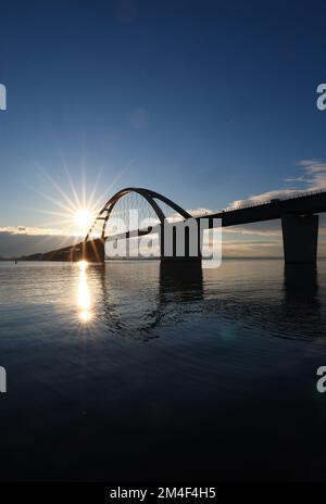 Fehmarn, Deutschland. 16.. Dezember 2022. Die Fahrzeuge fahren über die Fehmarnsund-Brücke unter blauem Himmel. Die Arbeiten an der Baustelle für den geplanten Ostsee-Tunnel in der Nähe von Puttgarden auf der Insel Fehmarn gehen voran. Der 18 km lange Straßen- und Eisenbahntunnel verbindet die Insel Fehmarn mit der dänischen Insel Lolland ab 2029. Laut Femern A/S belaufen sich die Kosten auf 7,1 Milliarden Euro. Kredit: Christian Charisius/dpa/Alamy Live News Stockfoto