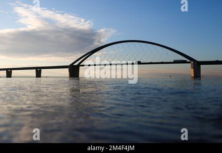 Fehmarn, Deutschland. 16.. Dezember 2022. Die Fahrzeuge fahren über die Fehmarnsund-Brücke unter blauem Himmel. Die Arbeiten an der Baustelle für den geplanten Ostsee-Tunnel in der Nähe von Puttgarden auf der Insel Fehmarn gehen voran. Der 18 km lange Straßen- und Eisenbahntunnel verbindet die Insel Fehmarn mit der dänischen Insel Lolland ab 2029. Laut Femern A/S belaufen sich die Kosten auf 7,1 Milliarden Euro. Kredit: Christian Charisius/dpa/Alamy Live News Stockfoto