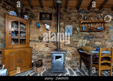 Kleiner Holzofen im Speisesaal eines rustikalen alten Landhauses mit Schieferwänden und Steinfußboden Stockfoto