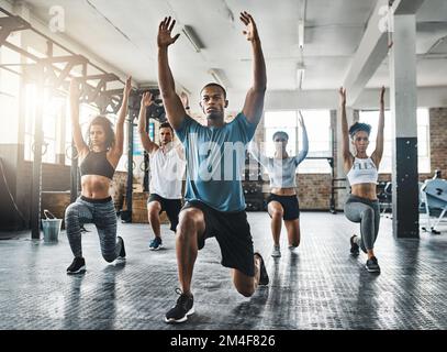 Dehnen sich über ihre Komfortzonen hinaus. Eine Gruppe junger Leute, die während ihres Trainings in einem Fitnessstudio Ausfallschritte machen. Stockfoto