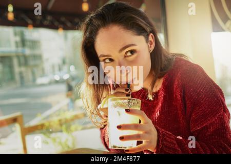 Jeder Schluck ist so etwas Ähnliches. Eine junge Frau, die ein frisches Getränk in einem Café genießt. Stockfoto